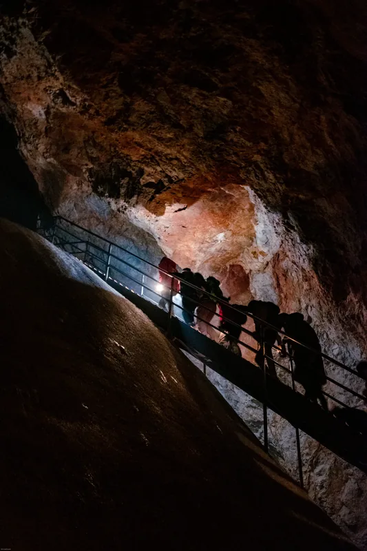 Visitors descending a railed path through a warm-lit cavern