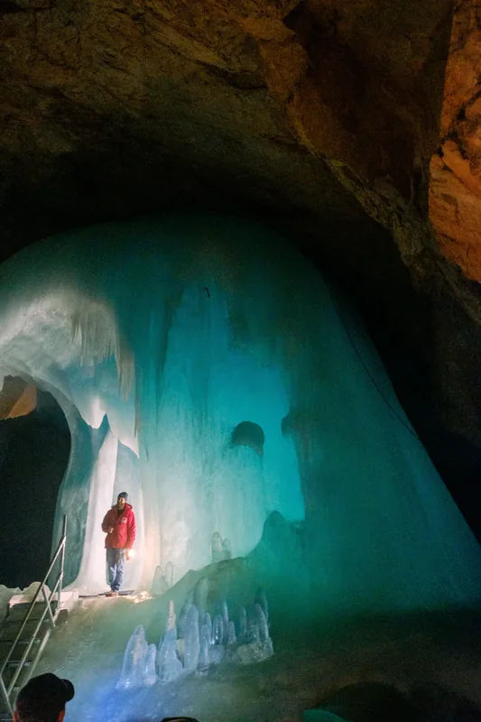 Figure in a red jacket inside a turquoise ice cave
